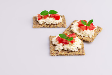Diet flax seed whole grain crackers with ricotta cheese, tomato and herbs isolated on white background, soft light