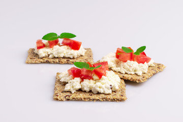 Diet flax seed whole grain crackers with ricotta cheese, tomato and herbs isolated on white background, soft light