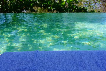 A  lue beach towel by a turquoise swimming pool