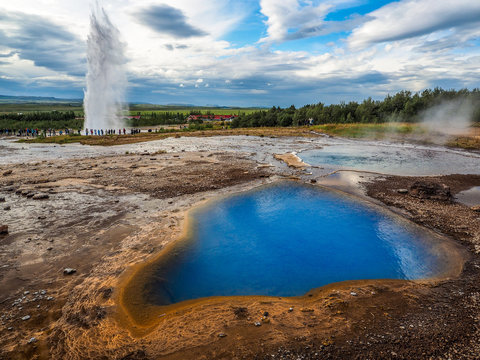 Strokkur Geyser erupting behind Blesi goethermal pool at Geysir. This is one of the three popular sights of the Golden Circle sightseeing circuit near Reykjavik city.