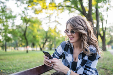 Atrractive blonde girl sitting in the park and reading text message on her phone.