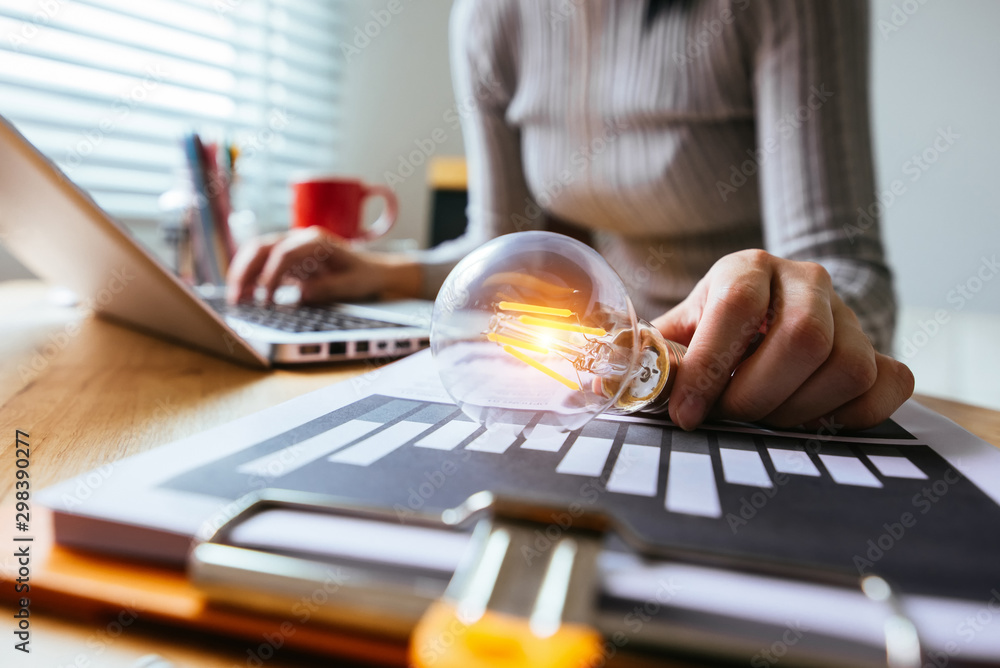 Poster business hand holding lightbulb with using laptop computer and money stack in office. idea saving en
