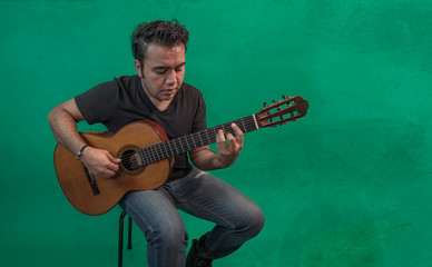 Obraz premium Young mexican with dark skin, latin playing guitar on green background