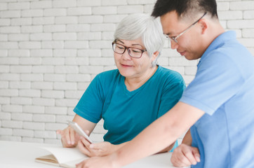 Obraz premium Happy Asian senior woman learning to use smartphone teach by her son with Gold fish in aquarium on white table, Happy day and good time family relationships concept