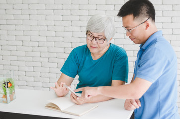 Obraz premium Happy Asian senior woman learning to use smartphone teach by her son with Gold fish in aquarium on white table, Happy day and good time family relationships concept