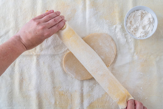 Woman’s hands on wood rolling pin, cloth covered, rolling out cookie dough on pastry cloth, small bowl of flour