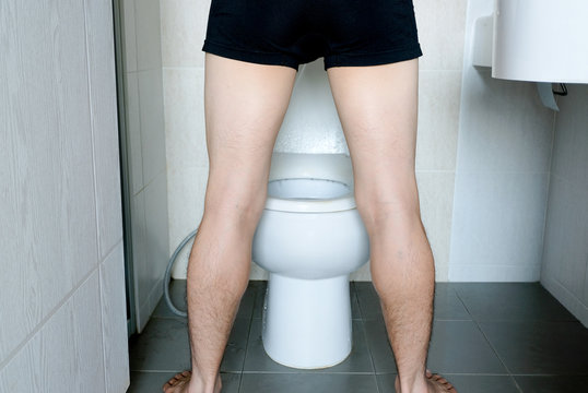 Rear view Leg of man standing peeing to toilet bowl in restroom at home  . Health concept