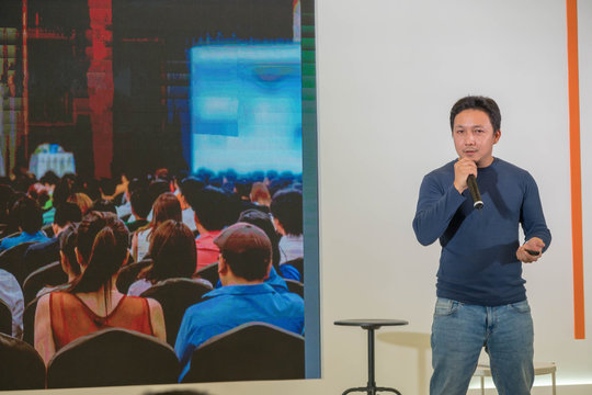 Asian Speaker is speaking on the stage over the presentation screen in the education seminar