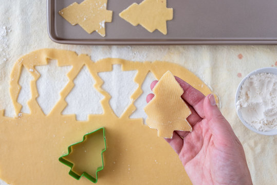 Woman’s hands cutting out Christmas tree sugar cookies, pastry cloth, cookie sheet