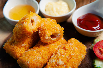 Crispy salmon cheese placed on a wooden chopping board with three dipping sauces, mayonnaise, tomato sauce, chicken sauce