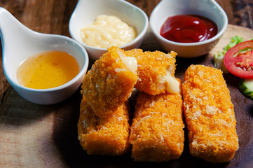 Crispy salmon cheese placed on a wooden chopping board with three dipping sauces, mayonnaise, tomato sauce, chicken sauce