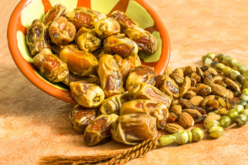 lots of fresh and healthy dates kept in a Arabian traditional pot and almonds and a religious Tasbeeh  kept of a marble table and ready to break fast in the holy month of Ramadan 