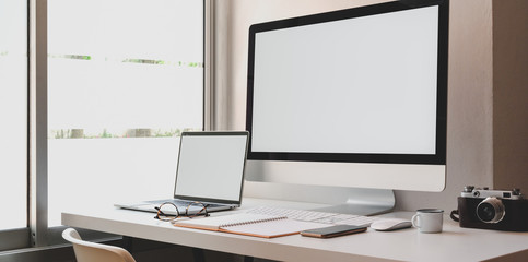 Blank screen desktop computer and laptop in modern workspace
