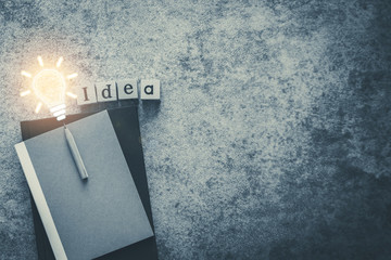 Cube letter word of Idea with notebook, sharp pencil and bulb light with copy space. Futuristic icon photo concept of business and education, thinking and problem solving, creativity invention.