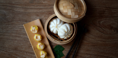 Overhead shot of Chinese steamed dumpling and steamed pork bun in a bamboo steamer with chopstick