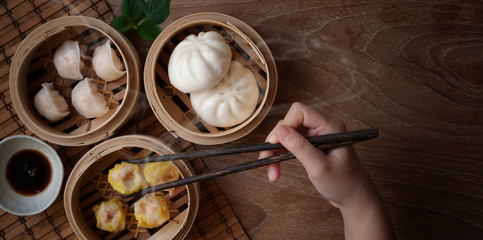 Fototapeta na wymiar Overhead shot of woman eating Chinese steamed dumpling and steamed pork bun in a bamboo steamer