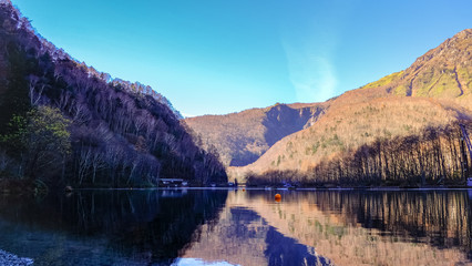 Landscape view of reflection water lake and hill trees blue sky background in fall autumn season at kamikochi Japan.