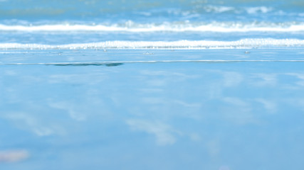 Beautiful soft wave with bubbles foams of clear blue water ocean sea on tropical sand beach with reflection of blue sky in thailand, vacation holiday nature background concept.