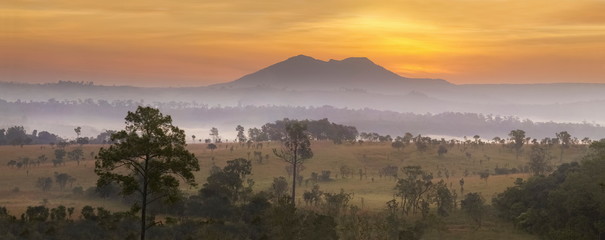 Mountain view panorama misty morning of peak mountain around with green forest and soft fog with yellow sun light in the sky background, sunrise at Thung Salang Luang, Khao Kho, Phetchabun, Thailand.