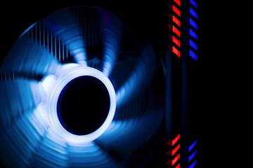 Fototapeta Fragment of the computer case. Powerful computer cooler in motion with blue backlight, next to the highlighted RAM red and blue.. obraz