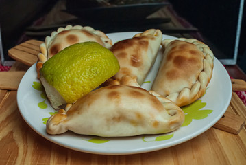 homemade Empanadas (detailed close-up shot; selective focus) typical of the Argentine countryside gastronomy, on white plate on rustic wooden table.