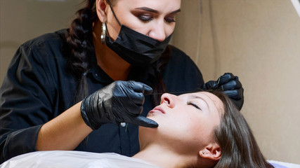 The process of shaping eyebrows by a beauty master with a thread for a young lady in the studio...