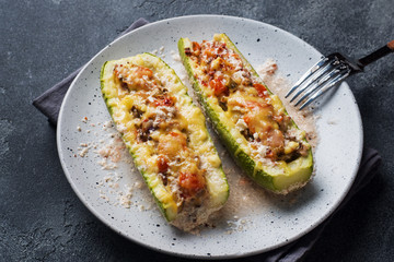 Baked stuffed zucchini boats with minced chicken mushrooms and vegetables with cheese on a plate.