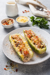 Baked stuffed zucchini boats with minced chicken mushrooms and vegetables with cheese on a plate.
