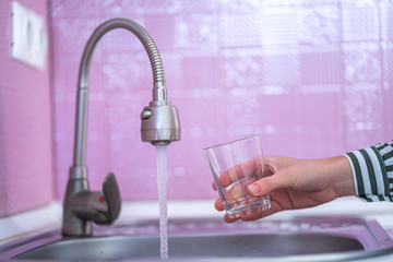 Female hands pouring tap water from faucet in glass for drinking at kitchen at home