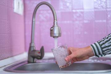 Female hands pouring tap water from faucet in glass for drinking at kitchen at home