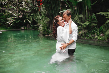 Happy couple kissing while relaxing in outdoor spa swimming pool surrounded with lush tropical greenery of Ubud, Bali. Luxury spa and wellness vacation retreat concept.
