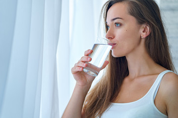 Happy attractive healthy drinking woman drinks clean purified glass of water in the morning in the kitchen at home. Healthy lifestyle