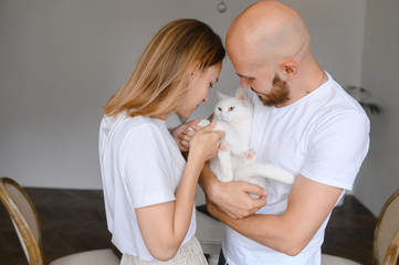 a young couple hold a white cat in their arms