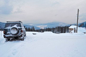 The car is covered with snow, parked in the background of a beautiful winter landscape