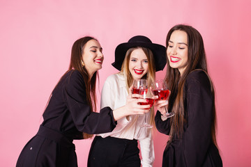 Three beautiful girls celebrate corporate party. Girls smiling and posing on pink background, bright makeup, red lips