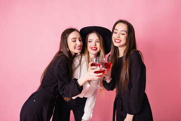 Three beautiful girls celebrate corporate party. Girls smiling and posing on pink background, bright makeup, red lips