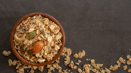 Obraz na płótnie Canvas Organic homemade Granola Cereal with oats,almond and pumpkin seeds in wooden bowl on dark background with copy space,ingredients for healthy food