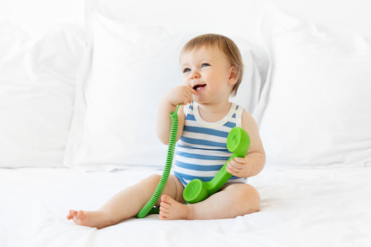 Cute smiling baby sitting on bed chewing on green phone