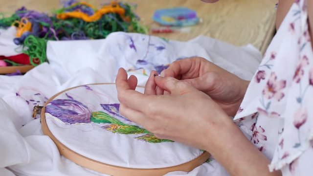 Female hands with vitiligo sewing with needle. embroidery hoop, embroidered fabric with colorful pattern. top view, close up. Traditional hobby, lifestyle. Needlework, handicraft