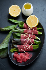 Rolls with carpaccio beef, salad leaves and grated parmesan on a black plate, studio shot over black stone surface