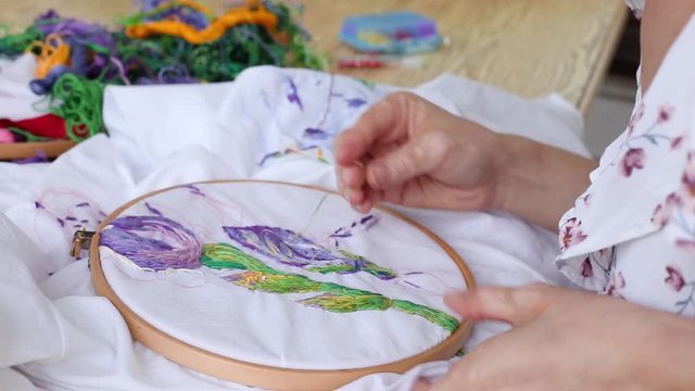Female hands with vitiligo sewing with needle. embroidery hoop, embroidered fabric with colorful pattern. top view, close up. Traditional hobby, lifestyle. Needlework, handicraft