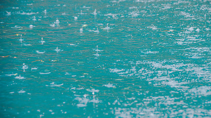 Raindrops on water surface of lake. The turquoise water of river. Rainy weather at sea