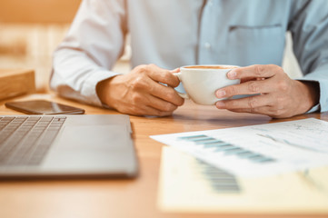 A young office worker is sitting and sipping coffee and relaxing in the afternoon. Relax after working all day and to continue starts working on documents and contacts business partners.