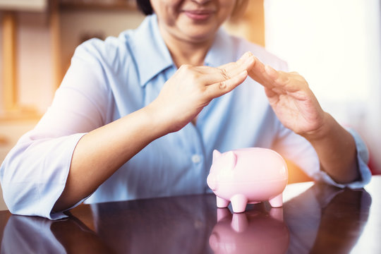 Asain Elder  Putting Coin Money To Piggy Bank Saving, Family, Savings, Age And People Concept - Smiling Senior Couple With Money And Piggy Bank At Home.