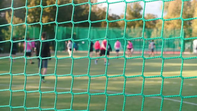 Close-up of a sports net. In the background they play football.