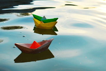 Colored paper boats in the water at sunset. Cardboard ships in a fountain in a city park. Children's natural paper toys