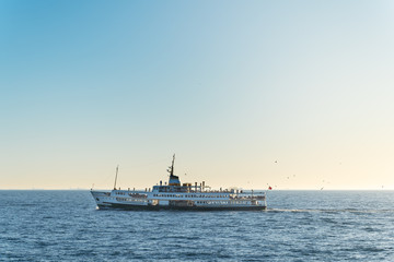 A pleasure ship with turkish flag, floats against the backdrop of emptyness of sea and silhoettes of bulk-carrier on the horizon.