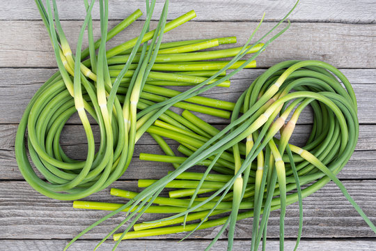 Green stalks of garlic on wooden table. The twisted stems of plants from seed. Preparation of summer salad for healthy diet
