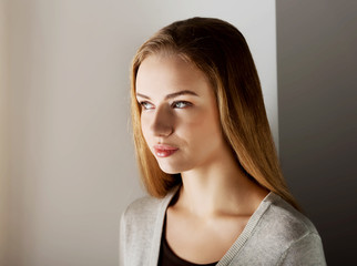 Obraz premium Dreaming woman standing near window in sunbeams. Portrait of blond woman.