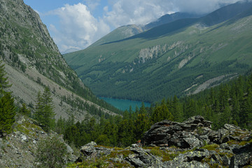 Mountain blue lake among rocks. Stone ridge in river valley under clouds. Travel in mountains among hills